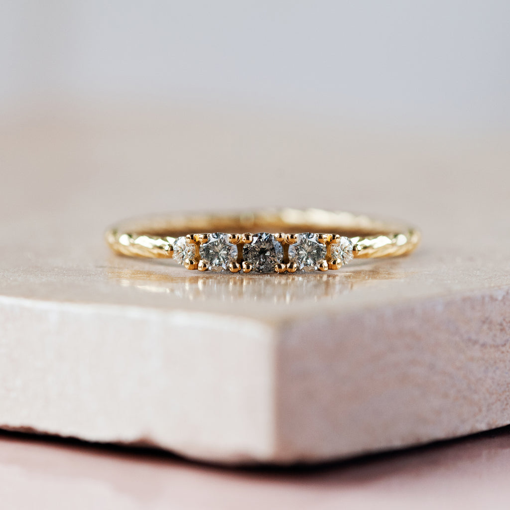 Salt & pepper diamond birthstone ring with two white diamond side stones on a textured gold band. 