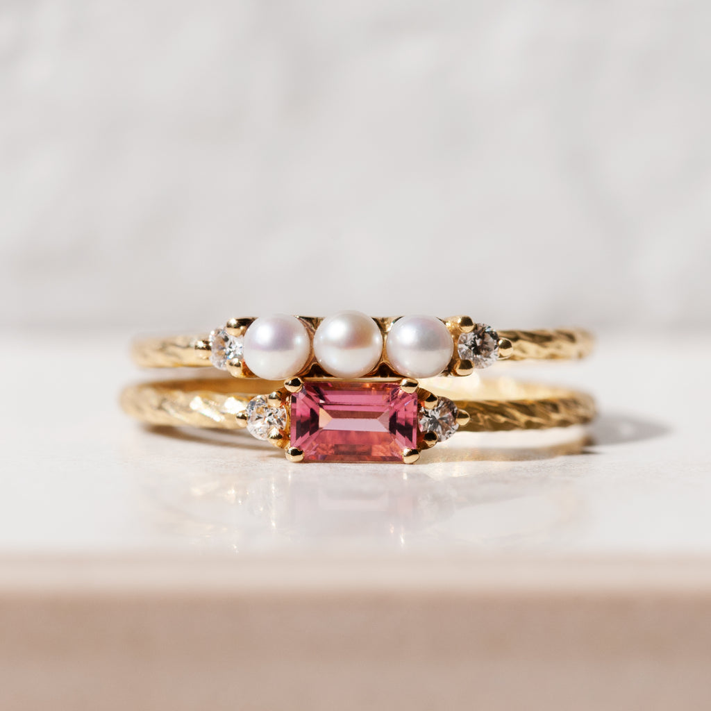 The pearl and tourmaline birthstone rings stacked on top of each other showing the gems and textured bands.