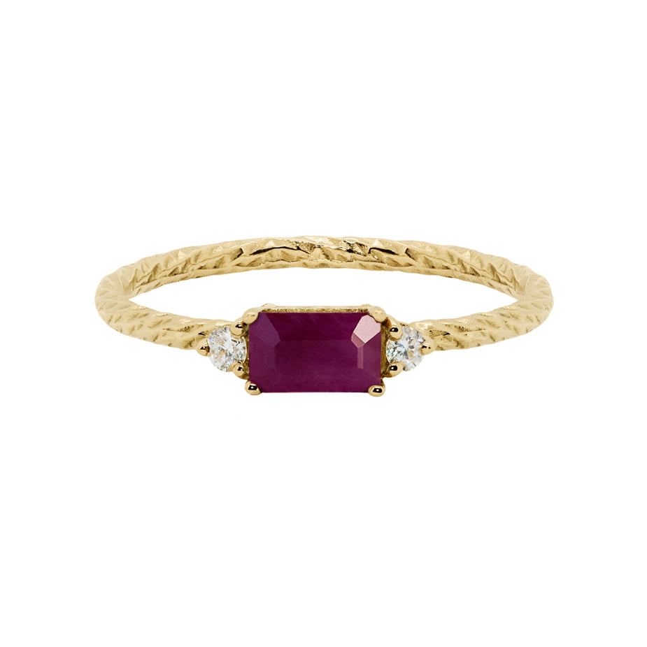 Ruby trilogy birthstone ring with two white diamond side stones on a textured gold band.
