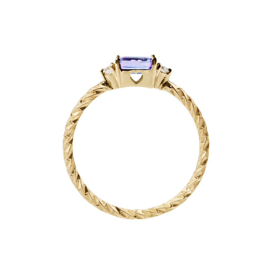 The tanzanite trilogy birthstone ring with two white diamonds on either side and a textured band. Sideview showing a cut out heart on the stone setting.