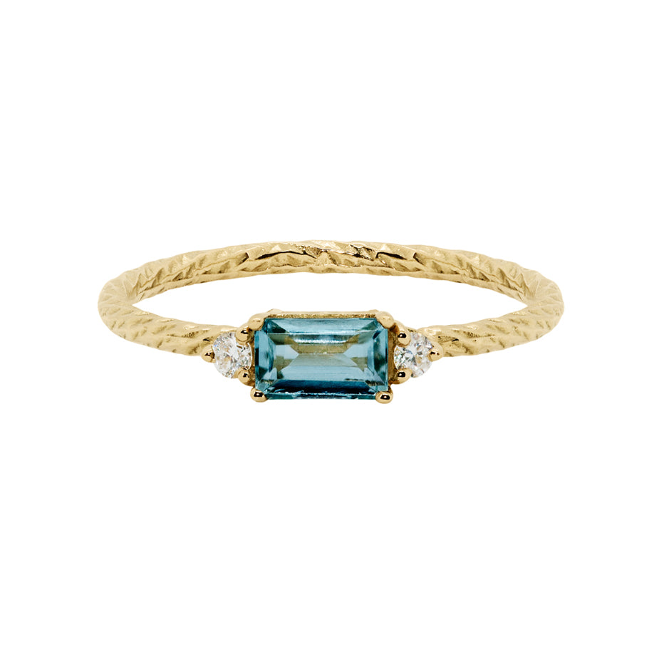 London blue topaz trilogy birthstone ring with two white diamond side stones on a textured gold band.