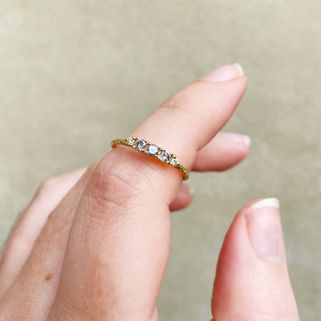 Salt & pepper diamond birthstone ring with two white diamond side stones on a textured gold band. Shown here on a hand.