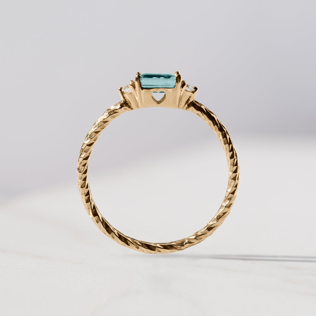 Aquamarine trilogy birthstone ring with two white diamond side stones on a textured gold band. Sideview showing a heart cut out in the stone setting.