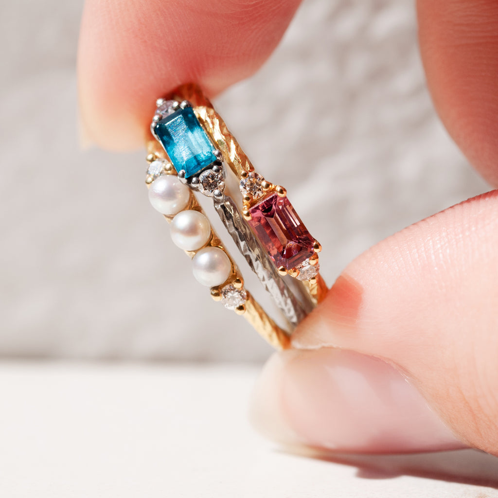 A close-up of the pearl, pink tourmaline and london blue topaz birthstone rings stacked together.