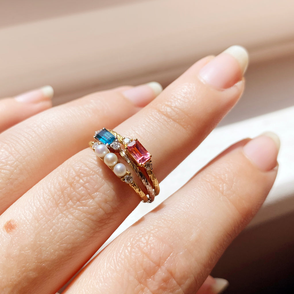 Shown are the pearl, tourmaline and topaz birthstone rings stacked together on a finger.