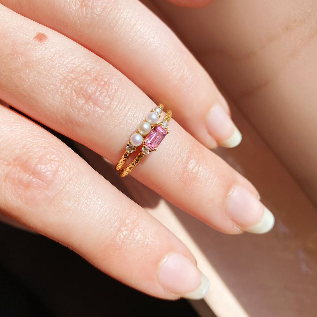 The pearl and tourmaline birthstone rings shown together on a finger.
