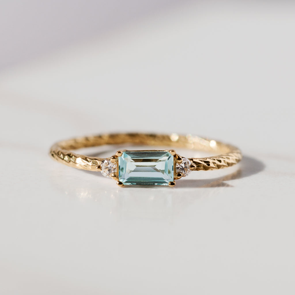 Aquamarine trilogy birthstone ring with two white diamond side stones on a textured gold band.