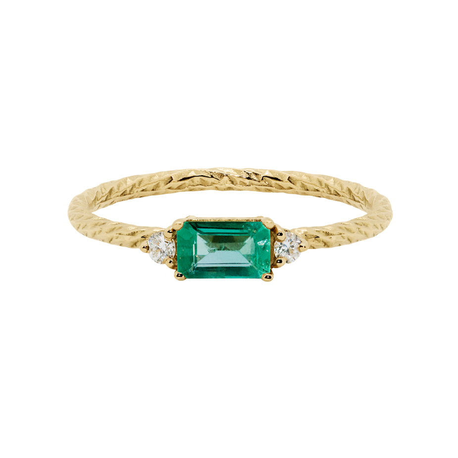 Emerald trilogy birthstone ring with two white diamond side stones on a textured gold band. 