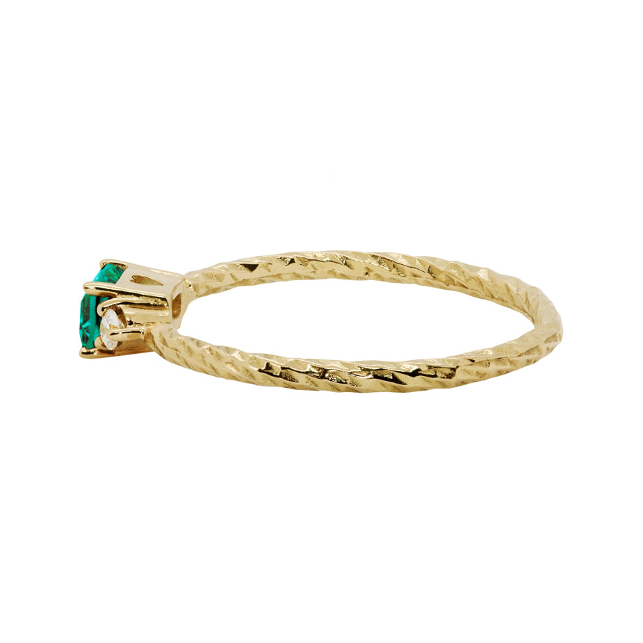 Emerald trilogy birthstone ring with two white diamond side stones on a textured gold band.
