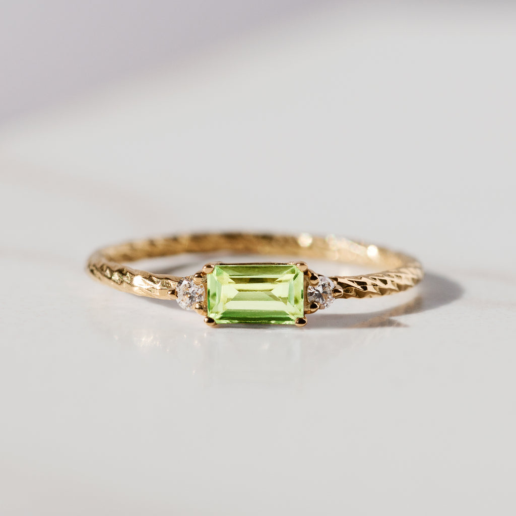 Peridot trilogy birthstone ring with two white diamond side stones on a textured gold band.